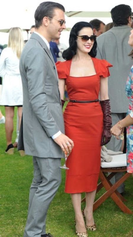 Theo Hutchcraft in a grey suit poses a picture with model Dita Von Teese.